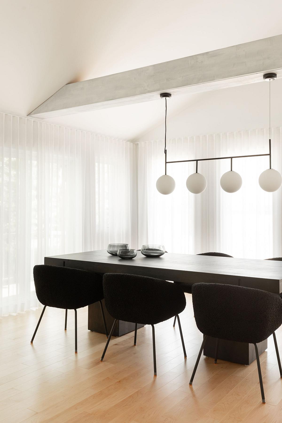 large, light and bright dining space with oak timber floorboards, ceiling beam supporting pendant light, sloped ceiling, sheer white curtains, a dark rectangle dining table with dark velvet dining chairs around it