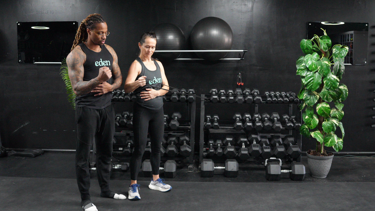 NASM-certified personal trainer Brandon Polk coaches a female client through internal and external shoulder rotations with a resistance band
