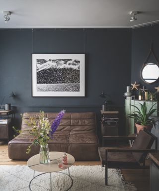 Black living room with large black and white abstract artwork on wall, pale wooden floorboards, cream deep pile rug and industrial furniture