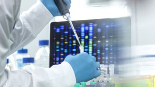 A man wearing gloves and a lab coat pipets a liquid into vials, with lab equipment visible in the background