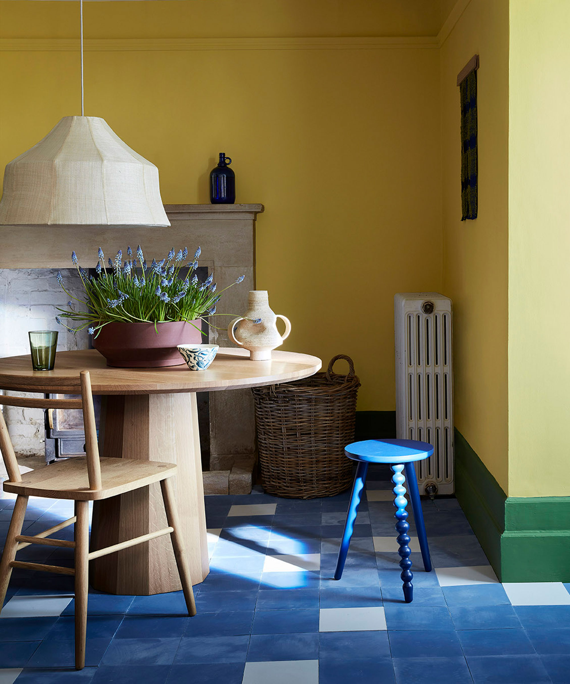 Colorful dining room space with yellow and green painted walls, blue tiled floor, light wood rounded dining table, blue bobbin stool, light wood dining chair