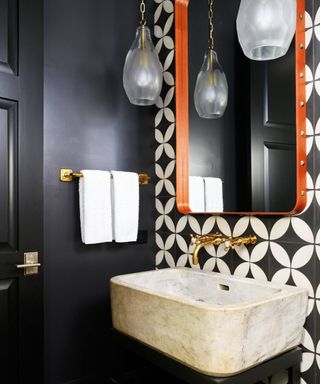 black bathroom with white and black accent wall tiles, orange mirror, marble sink, glass pendant lights