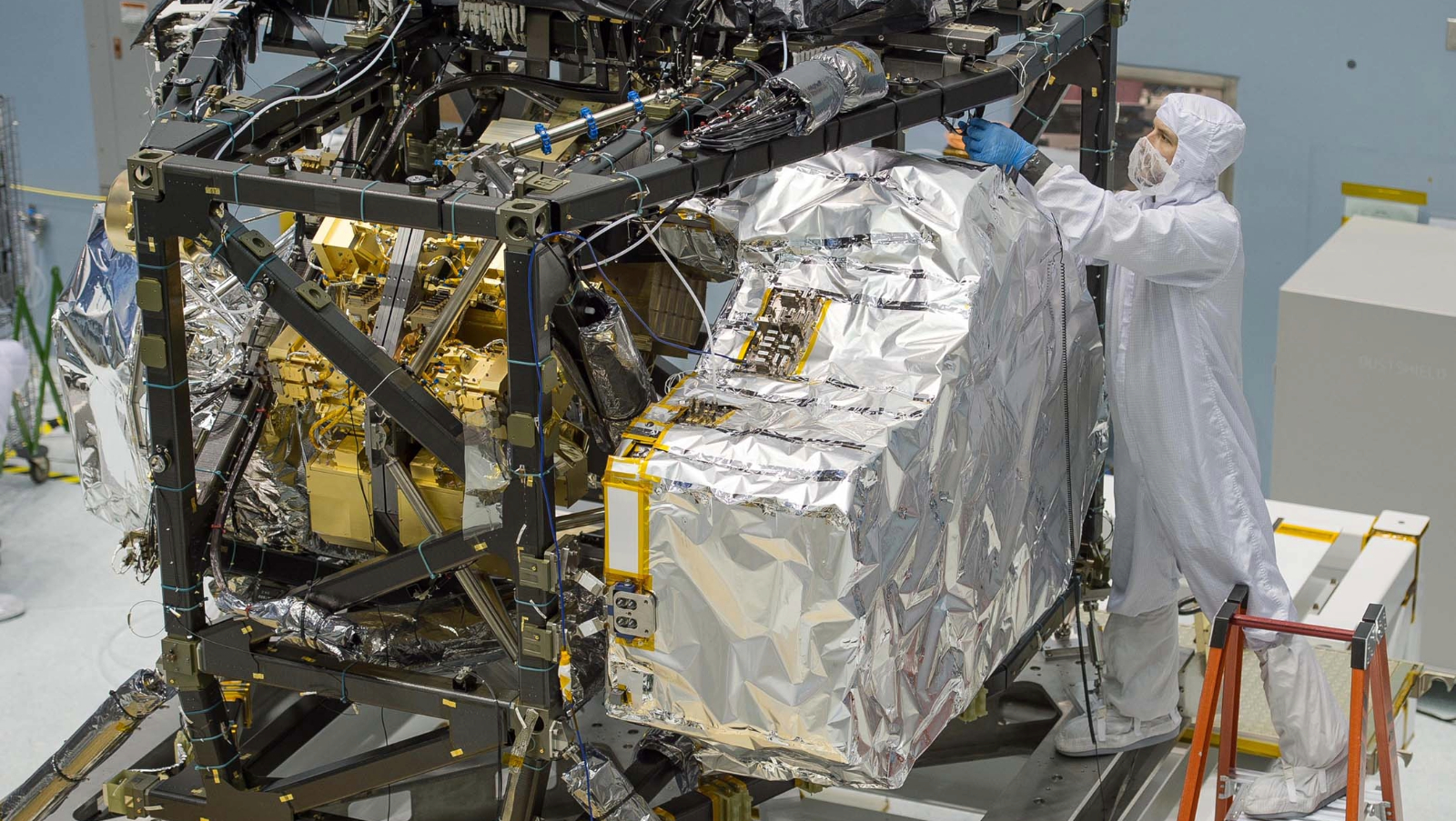 A person wearing white stands next to a large machine covered in foil.