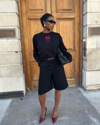 Marilyn wears black sweater, black tailored shorts and heels