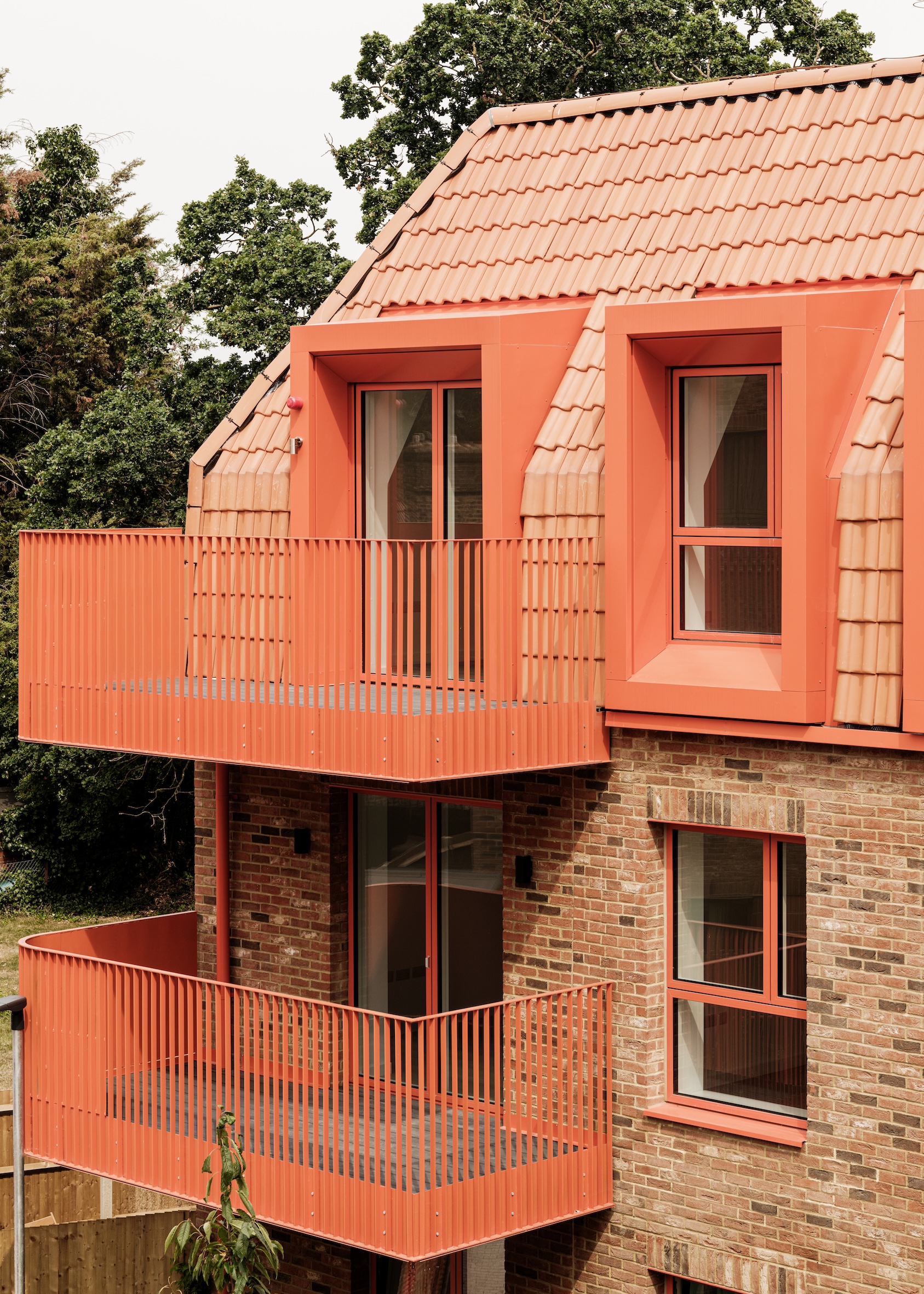 view of Farmstead Road, a brick residential complex in south london by metropolitan workshop. it features green gardens and orange metal details such as window frames and balconies