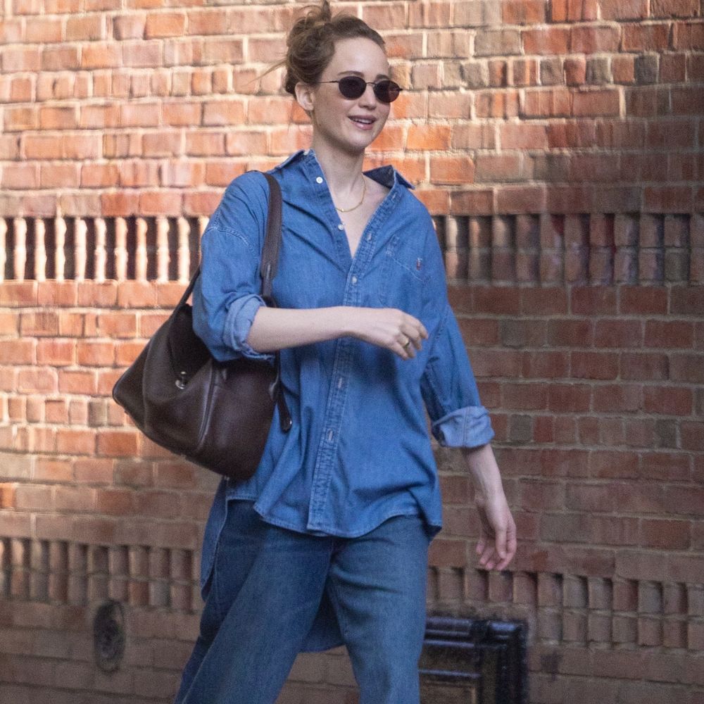 Jennifer Lawrence walks down the street in New York wearing baggy blue jeans with a denim skirt and bright blue shoes.
