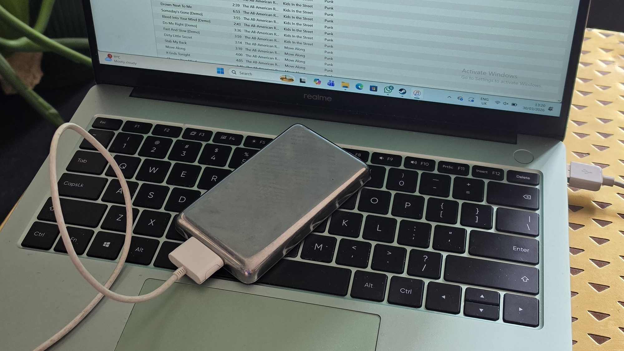 The iPod Classic connected to a green Realme laptop, showing iTunes.