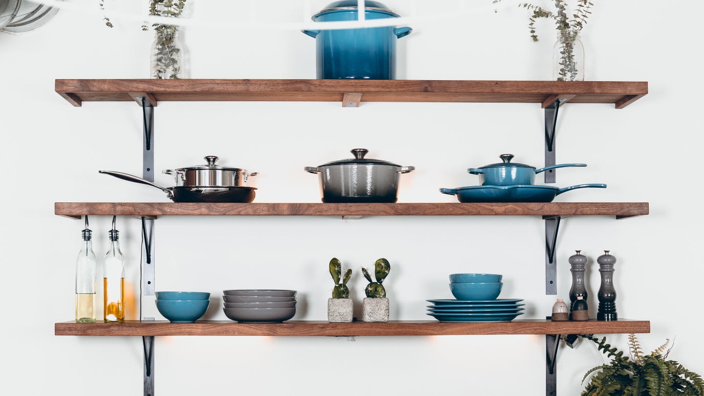 Kitchen wall with three wooden shelves with pots, pans, bowls and plates on it