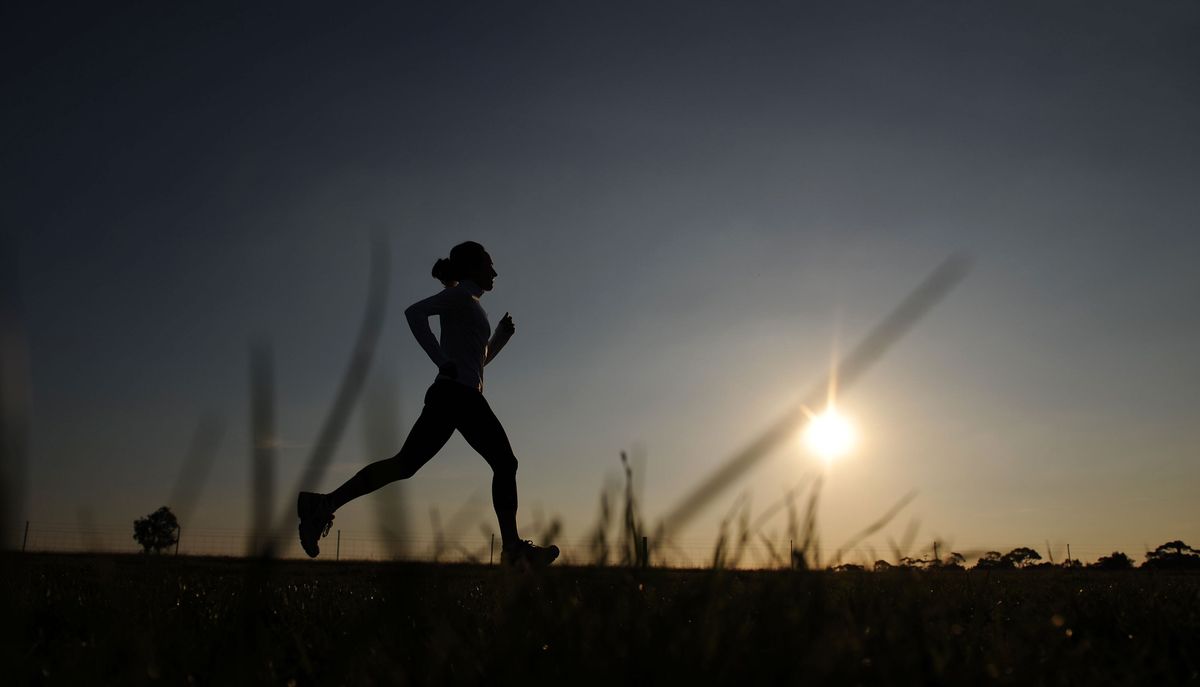 The silhouette of a woman running across fields at sunrise 