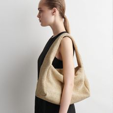 Woman wears black dress and raffia shoulder bag