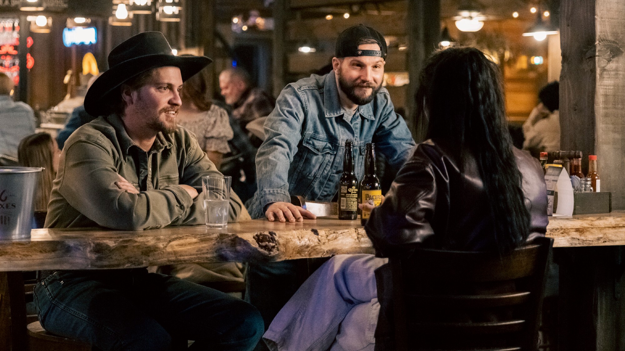 From left to right: Kayce and Cal smiling at Andrea in Marshals. They're sitting in a bar.