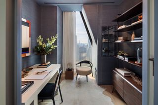 Home office with dark blue walls, long white desk, armchair by window and sheer curtains