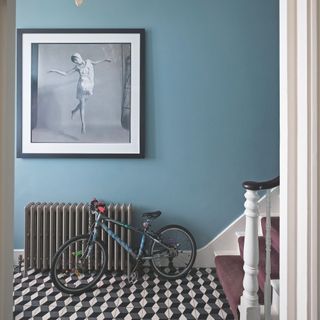 Blue hallway with white and black tiles and a cast iron radiator with a bike leaning against it