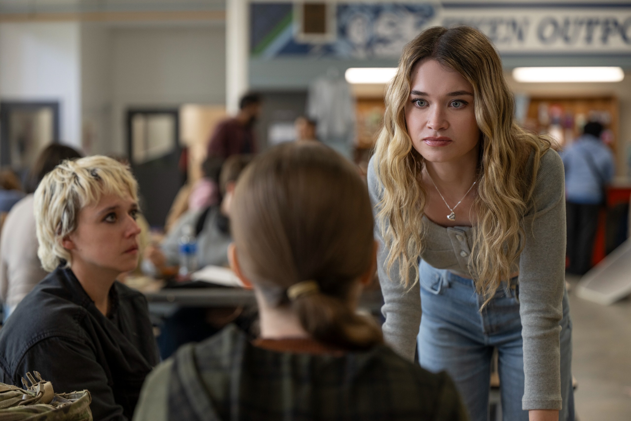 Alison Thornton as Chris leans over a school lunch table to threaten summer h. howell as carrie A third girl with a bleach-blonde pixie cut (Thalia Dudek as Emaline) looks on in 'Carrie'.