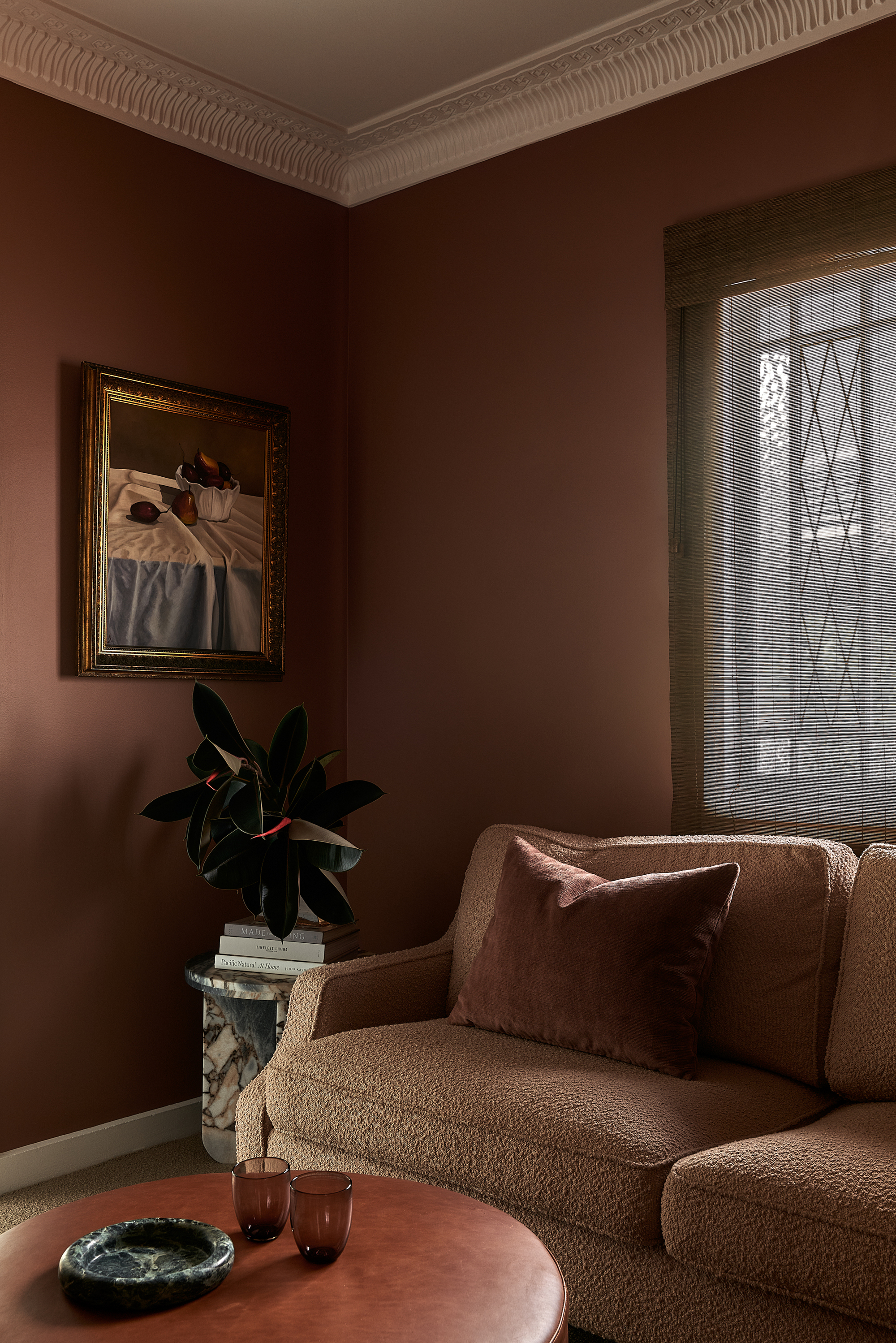 Image of the corner of a brown living room with cream molding. There is a light brown boucle sofa with a gray marble side table next to it, with a magnolia bouquet on it. There is also a wooden coffee table in front of the sofa.