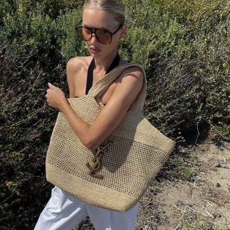 Elsa Hosk wears a black halterneck top, white trousers and carries a raffia Saint Laurent Icare bag