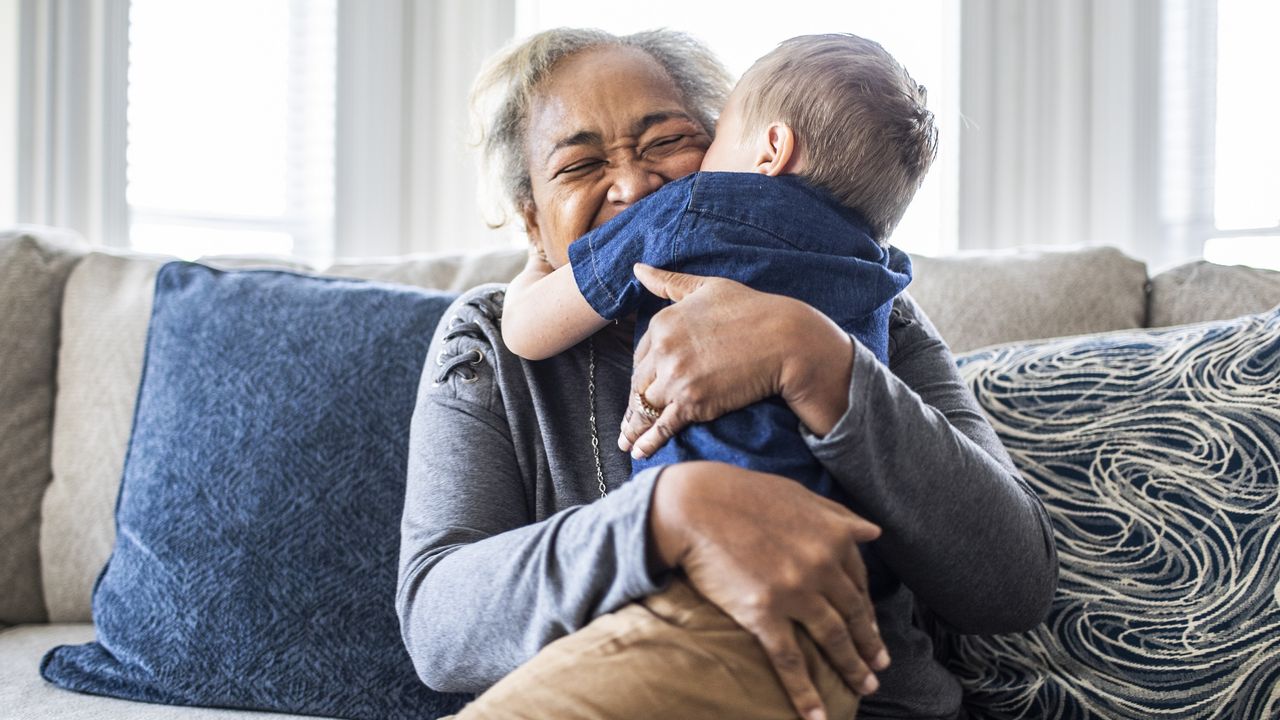 An older woman and a young boy happily hug each other on a sofa.