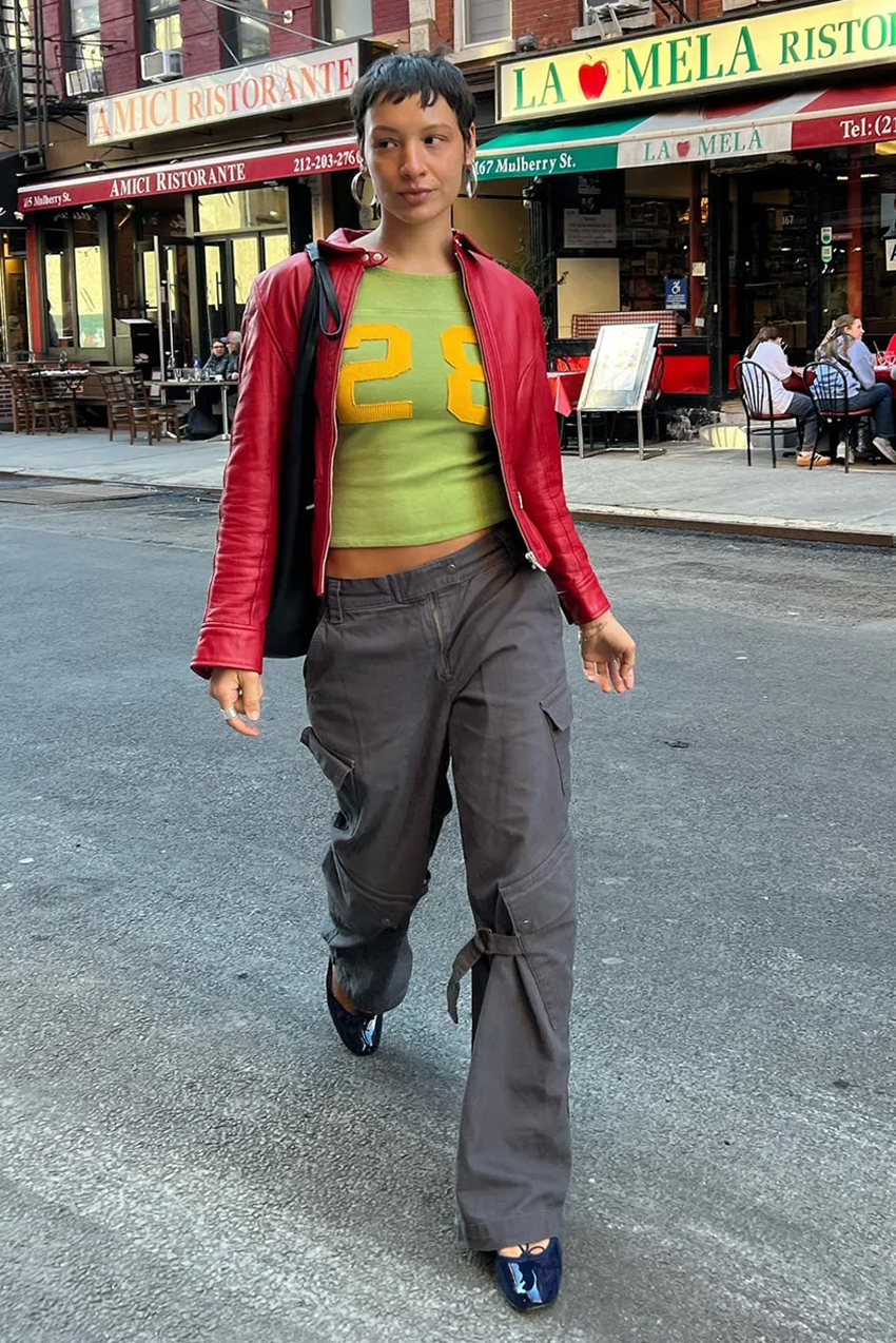 a woman wearing a red jacket, green jersey shirt, and gray pants