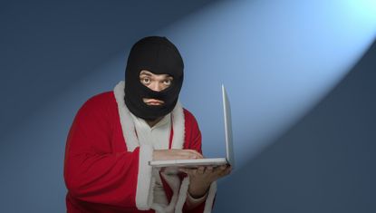 Balaclava-clad man in Santa suit, holding laptop