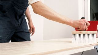 Man applying wallpaper paste to lining paper on pasting table with wooden wallpaper paste brush