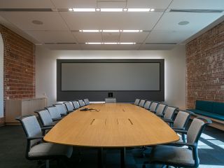 Square Boardroom featuring 32:9 Screen Innovations projection screen, Panasonic PT-RZ120LWU projectors, Meyer UP-4 slim speakers, Crestron Saros 2-Way In-Ceiling Speakers, Sennheiser Team Connect microphones, and Logitech Rally camera.