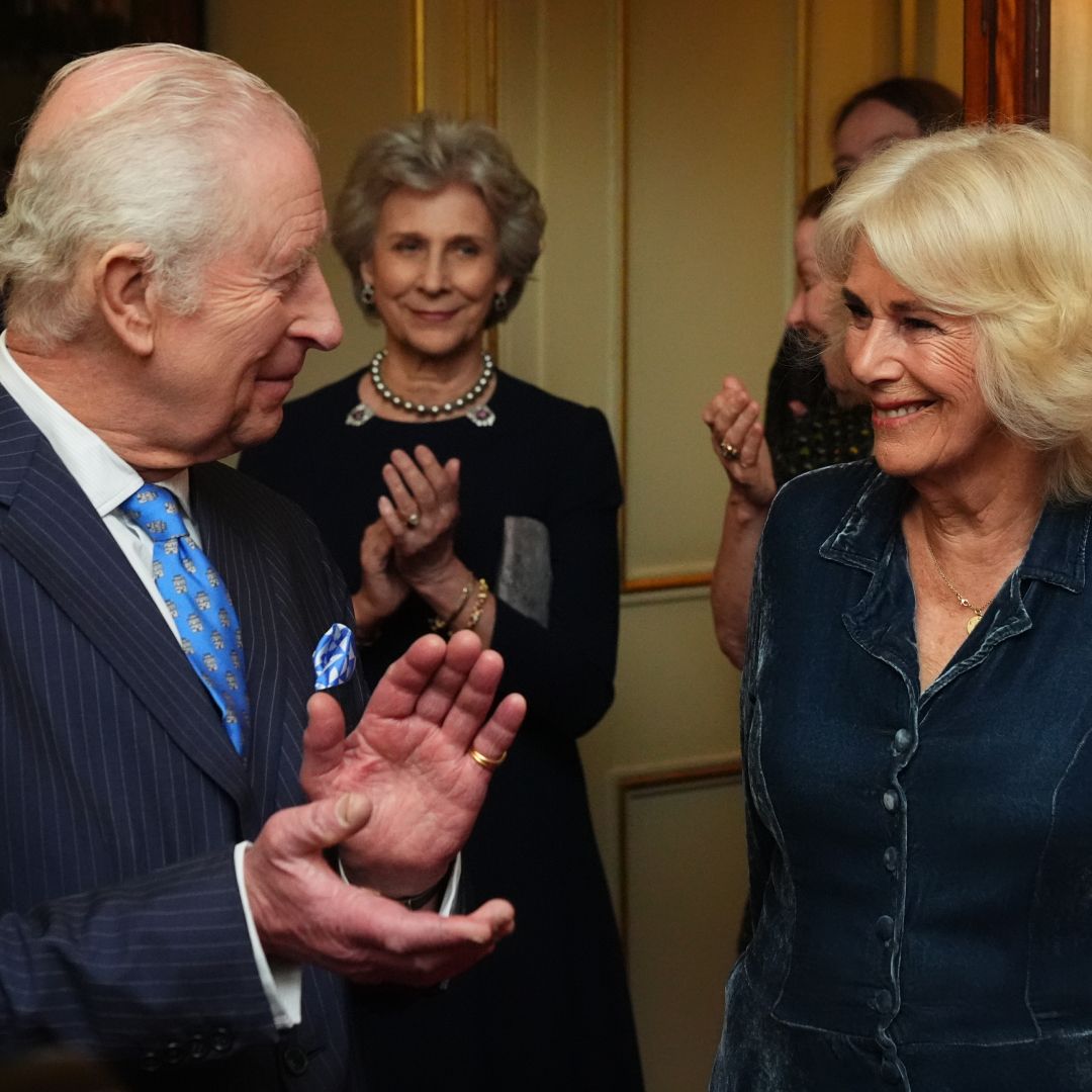 King Charles clapping and smiling at Queen Camilla, who is dressed in a blue dress