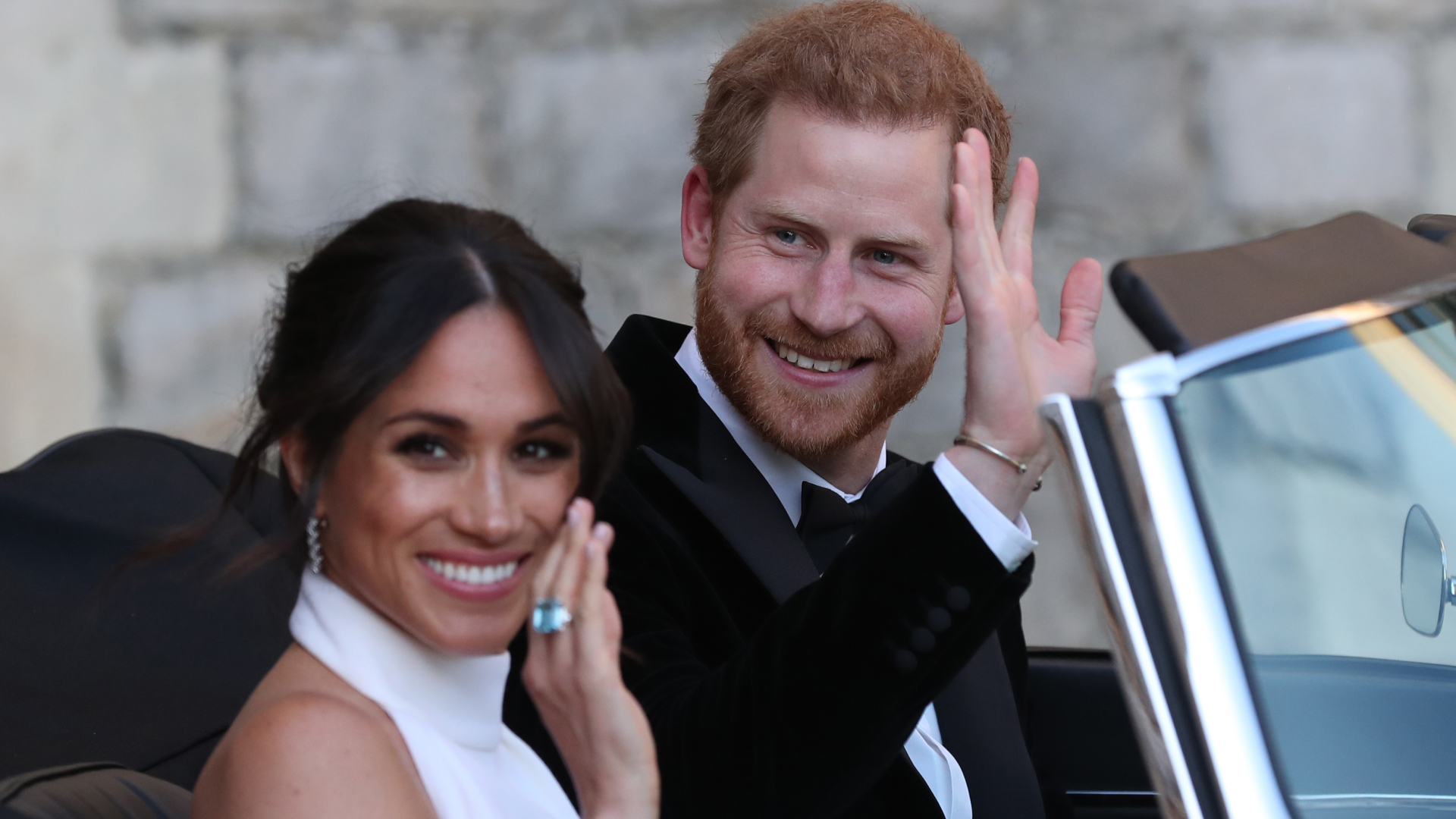 Prince Harry and Meghan Markle waving while driving to their wedding reception in a convertible
