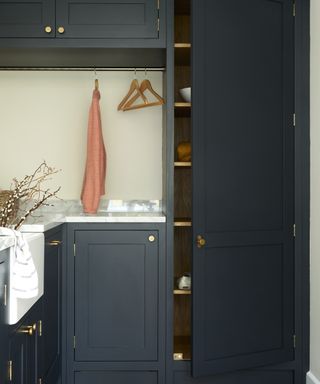 A smart navy laundry room with Shaker-style cabinetry, brass handle fixture decor and marble countertop