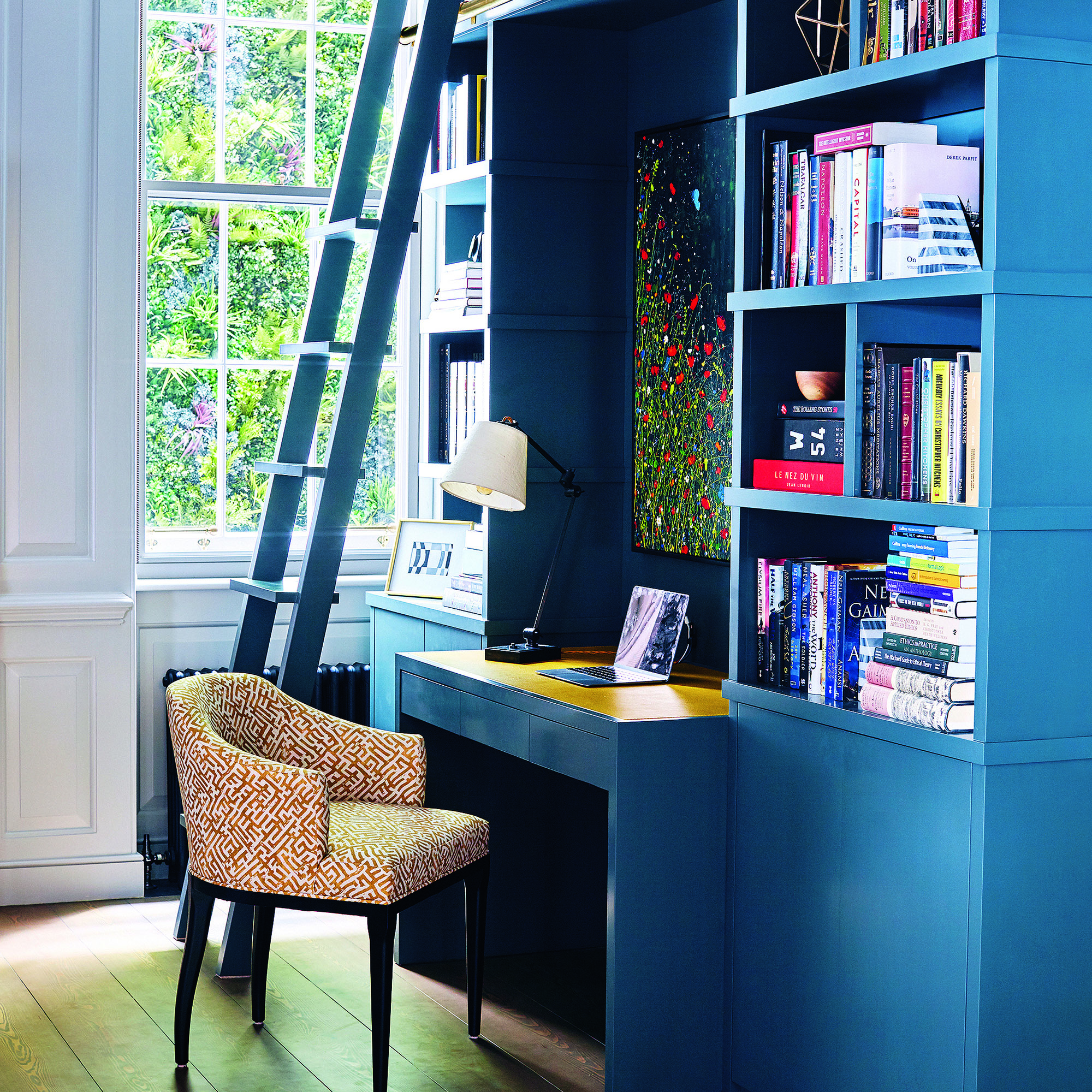 Home office with blue built in desk and shelving with wallpapered alcove.