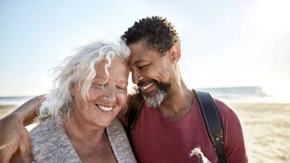 A retired couple walk arm in arm on the beach