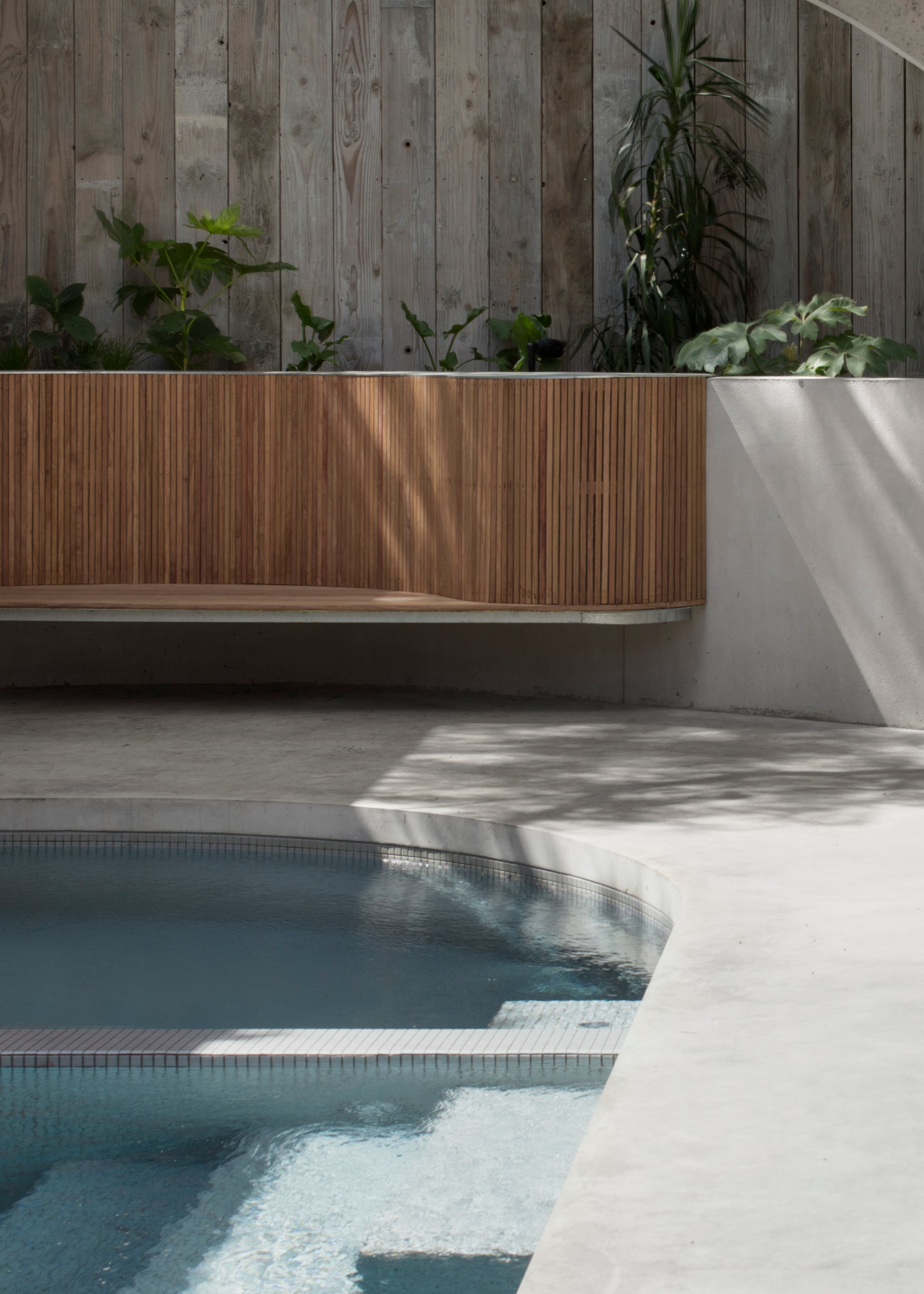 An outdoor pool with in-built seating on the deck and a brown wood fence