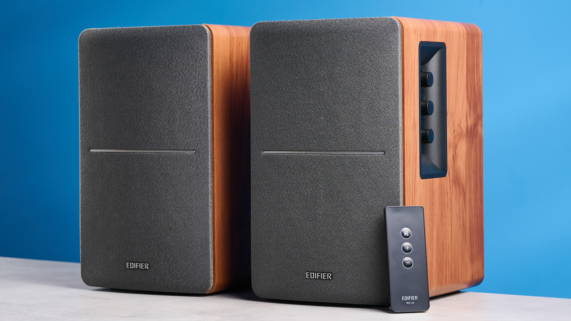 the edifier r1280t bookshelf speakers in wood brown photographed against the blue background, showing the volume adjustment dials, internal drivers and tweeters, RCA and aux inputs, and remote 