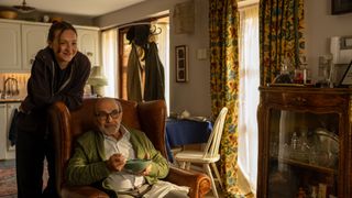 Ludmilla Makowski as Sandrine stands behind David Suchet who is seated eating soup as George in The Au Pair.