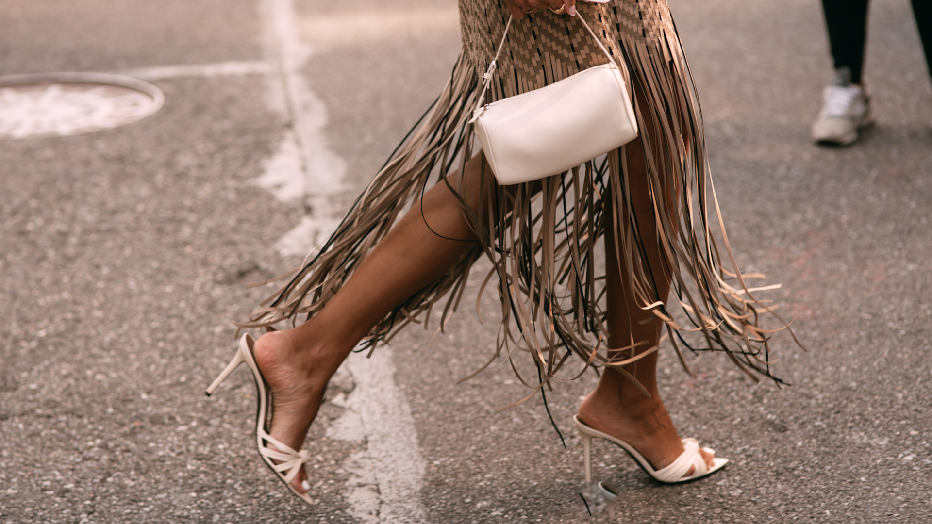 Woman crossing the street wearing fringe dress and white bag with white heels 