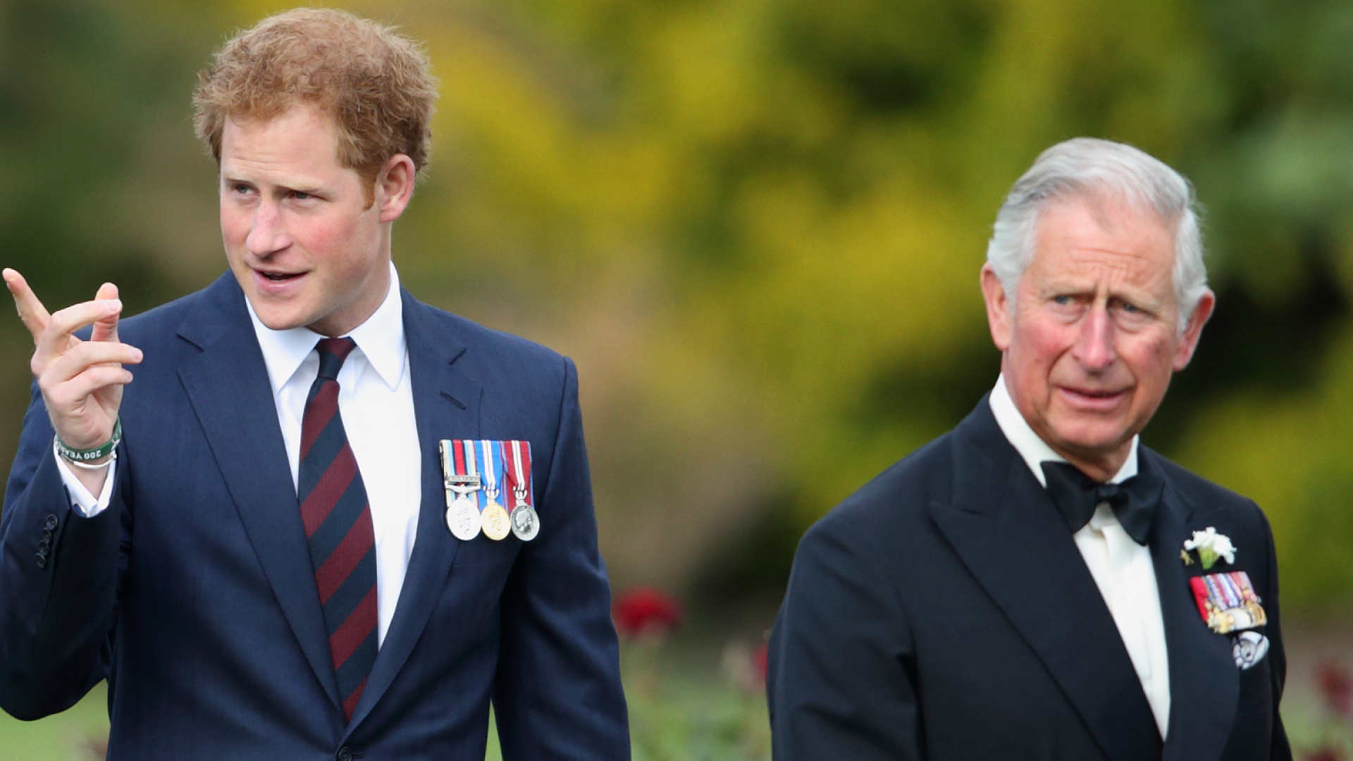 Prince Harry wears a suit with military medals and points while dad King Charles looks on while wearing a tuxedo