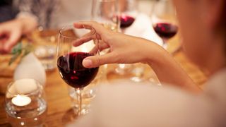 Woman holding glass of red wine at dinner table, one of the examples of healthy alcohol