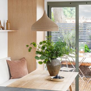 wooden dining table with plant and bench seating next to terrace