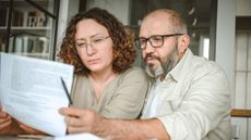 A mature couple reviews paperwork while sitting at their dining table.
