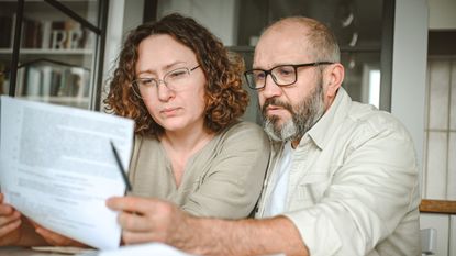 A mature couple reviews paperwork while sitting at their dining table.