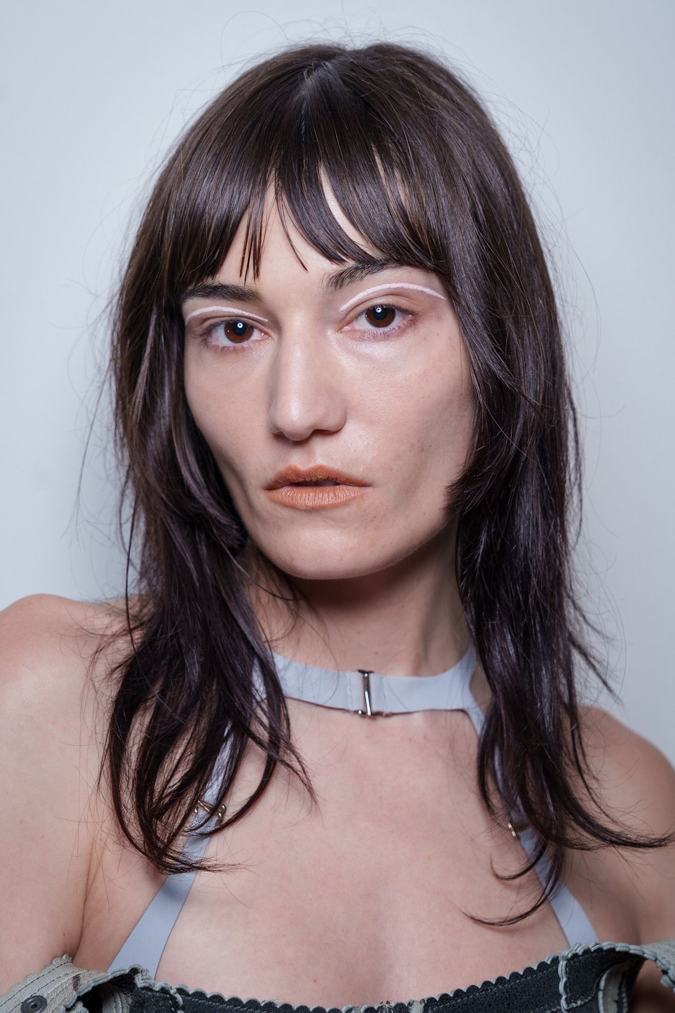 A model at KNWLS SS26 with a fringe hairstyle and graphic white eyeliner
