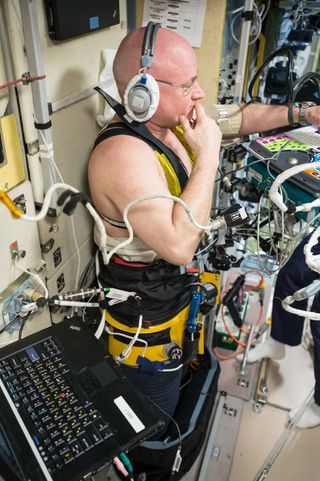 a shirtless bald man strapped to computers wearing headphones
