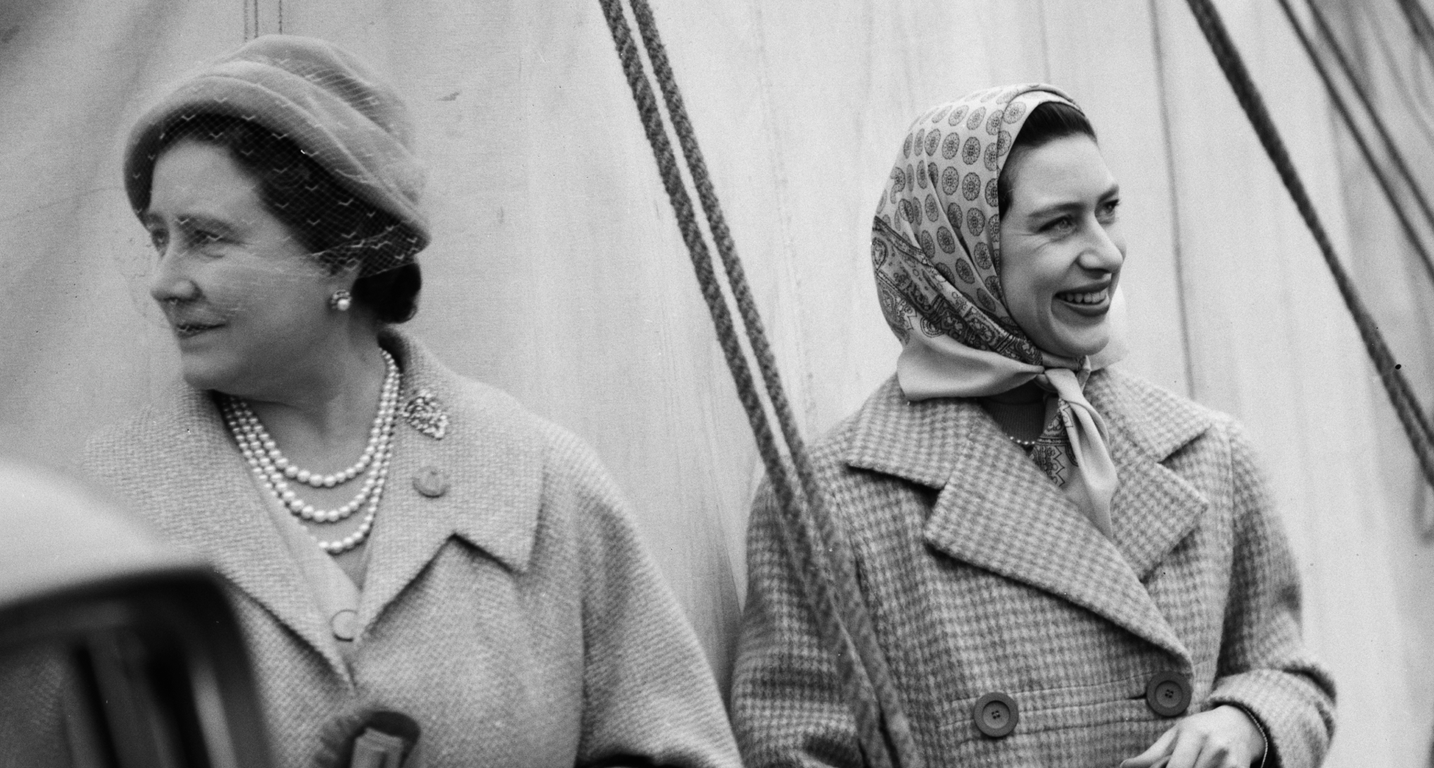 Princess Margaret wearing a headscarf standing next to the Queen Mother, looking away