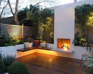 small patio with wooden deck, outdoor fireplace, seating and raised beds with up-lit bamboo
