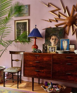 corner of room with lilac wall, wooden vintage sideboard and chair, eclectic maximalist decor