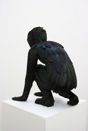 Crouching man covered in black feathers