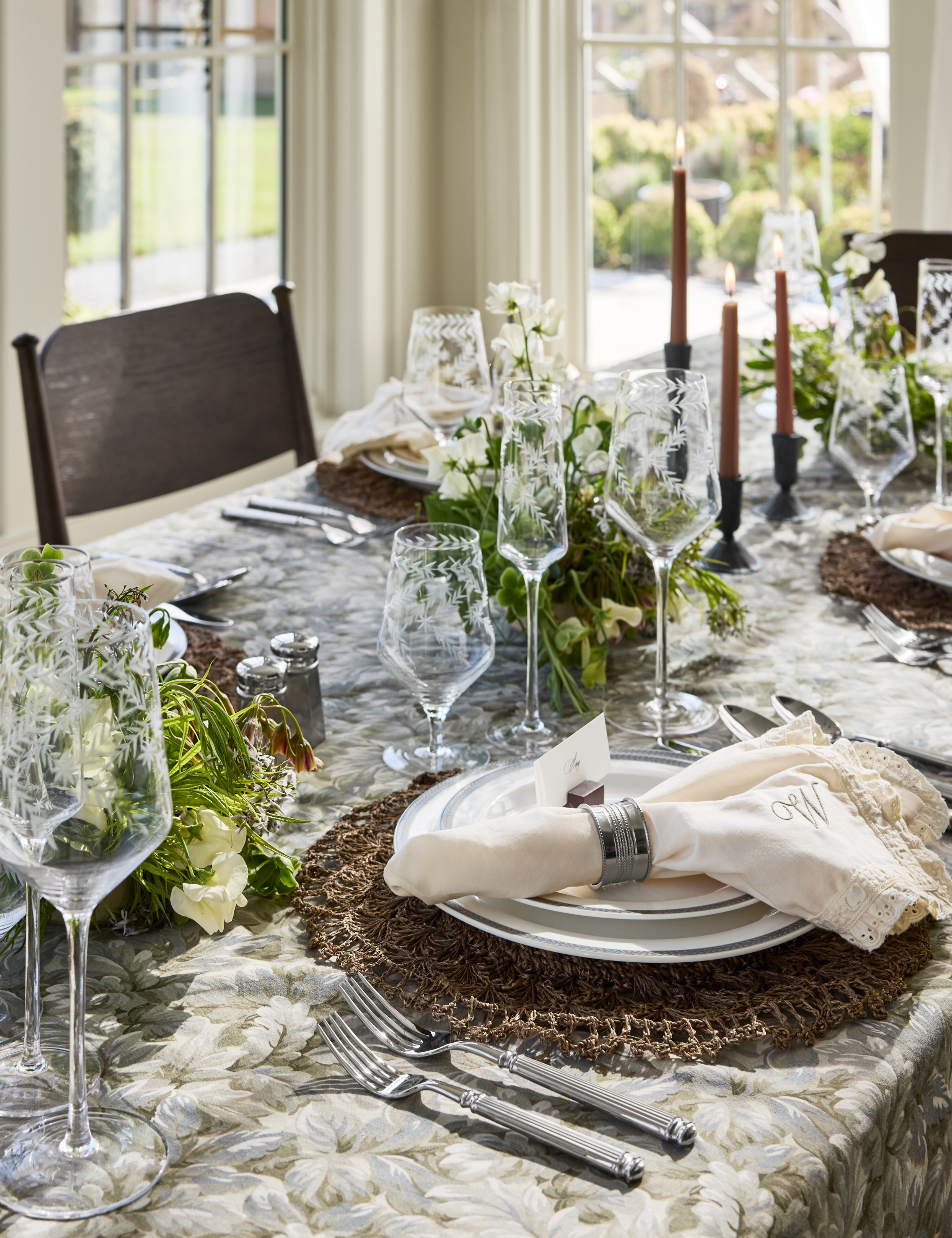 Bright fall dining table styled with a tapestry-inspired verdant tablecloth, fluted cutlery, textured placemats, and eyelit lace napkins.