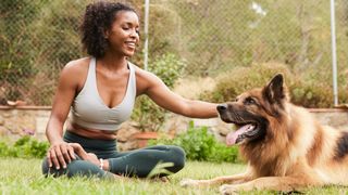 Young African American woman sitting on grass petting German Shepherd