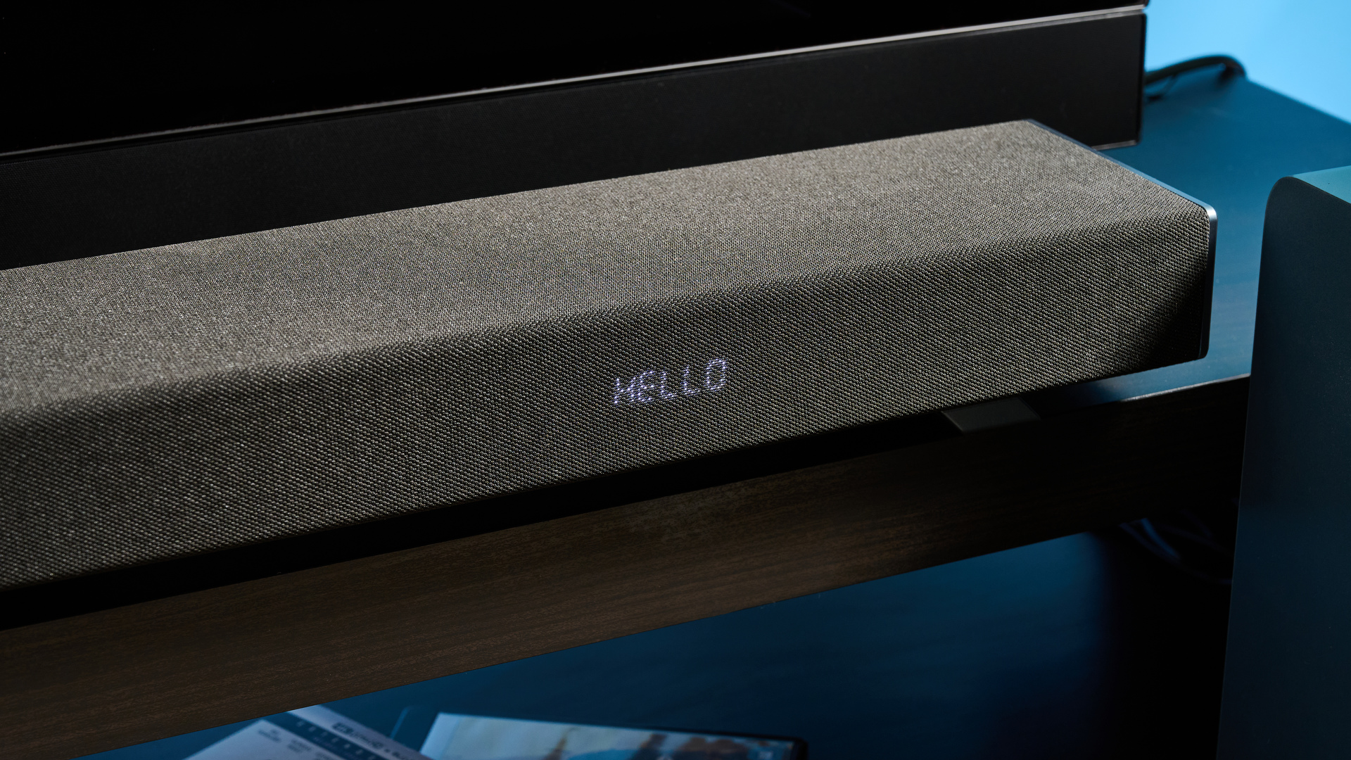the Sharp 3.1.2 HT-SBW53121 Soundbar in black with a remote, subwoofer, against a blue background next to a panasonic TV