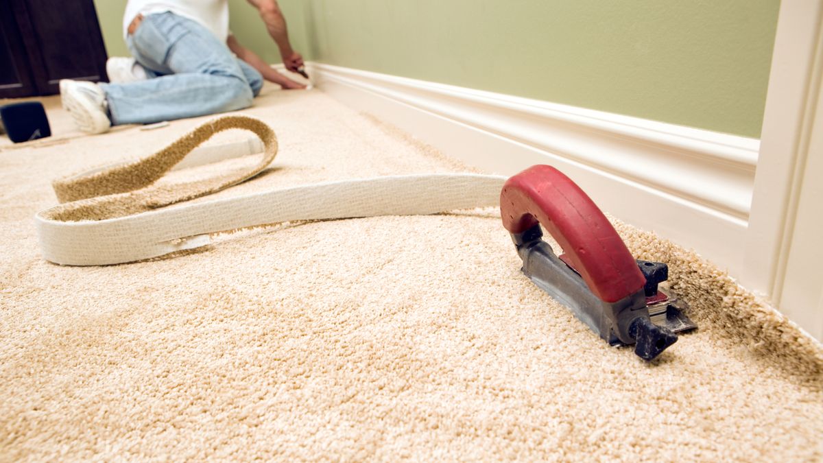 close up of cream carpet and tool in room being fitted by man kneeling in the background