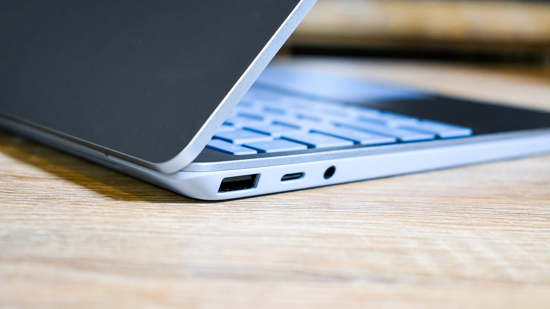 Surface Laptop Go yang setengah terbuka berbalik dan duduk di atas meja kayu